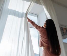 une femme ouvre les rideaux, le soleil est vif par la fenêtre